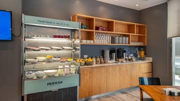 A modern kitchen area with a food display case, wooden shelves, and a dining table.