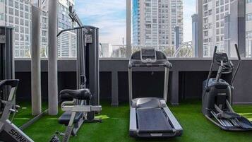 A gym with treadmills, elliptical machines, and a stationary bike, featuring a city view through large windows.