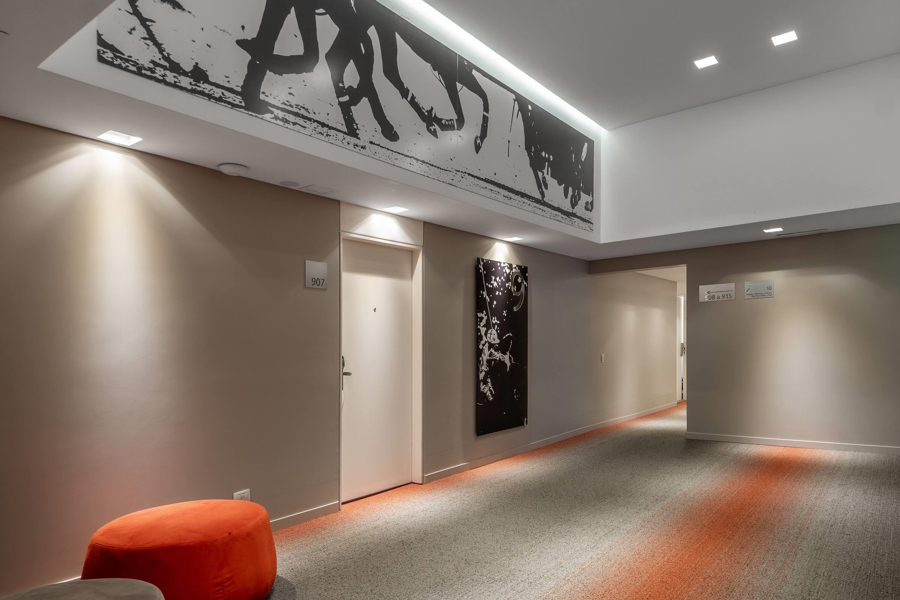 Un pasillo de diseño moderno con una gran obra de arte abstracta en la pared, una luz brillante en el techo y suelo alfombrado.