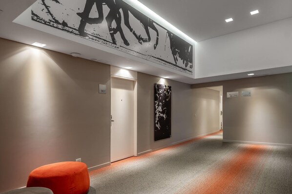 A hallway with a modern design, featuring a large abstract artwork on the wall, a bright overhead light, and a carpeted floor.