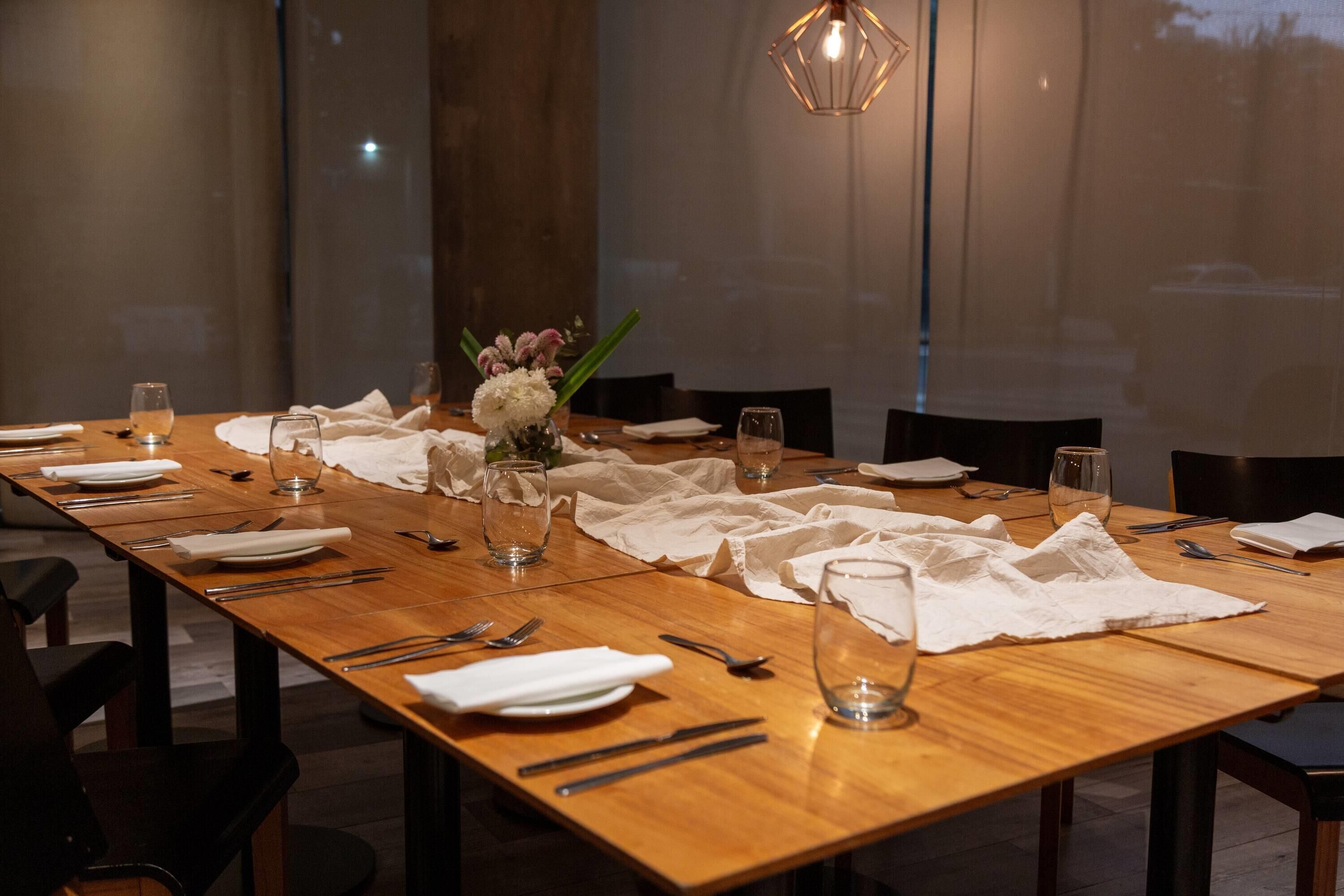 A long wooden dining table set for a meal with white napkins, cutlery, and glasses.
