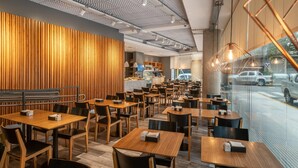 Ein modernes Restaurant mit Holzwandverkleidung, mehreren Tischen und Stühlen und Blick auf die Straße durch große Fenster.