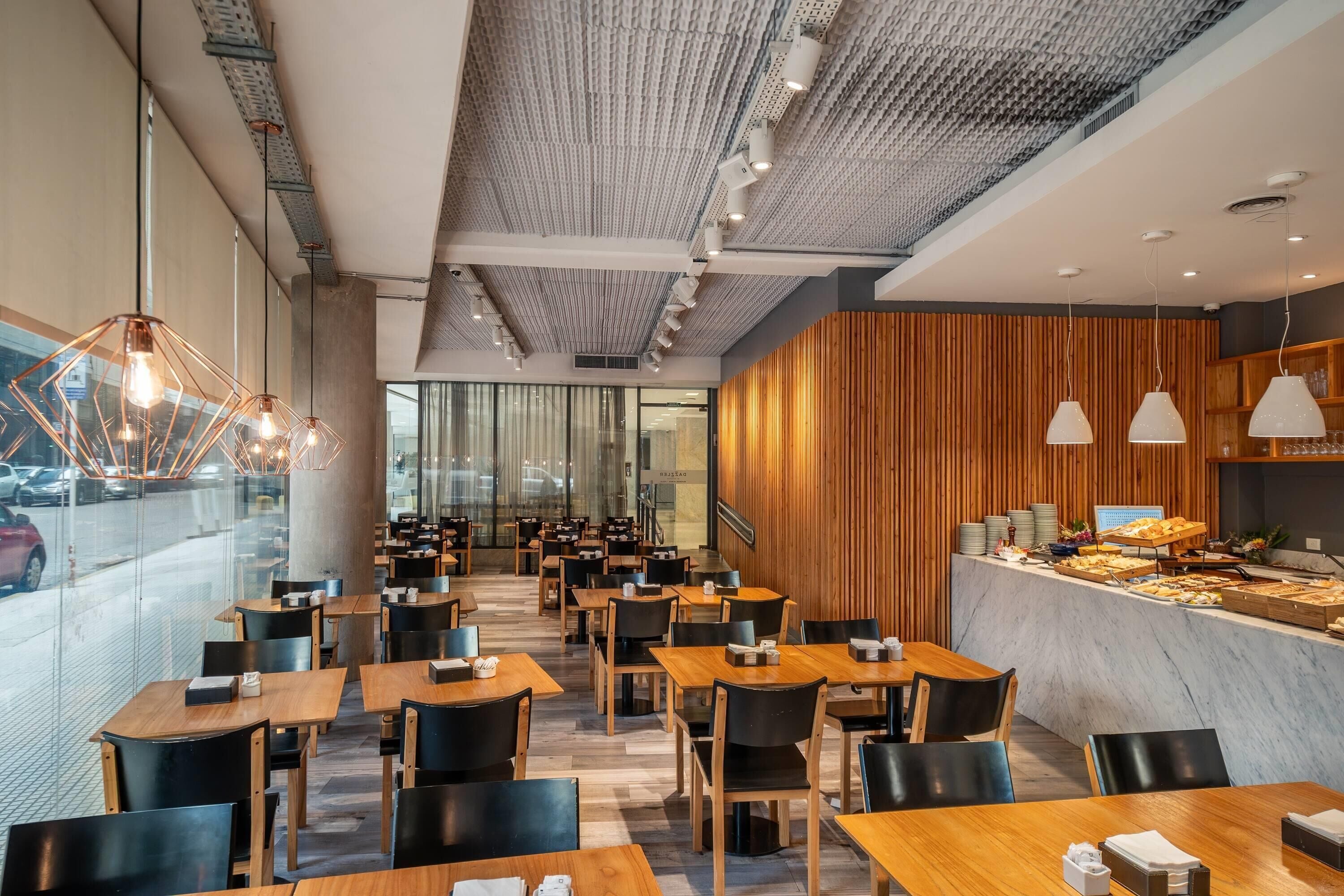 A modern restaurant with wooden tables and chairs, a counter with food display, and pendant lighting.