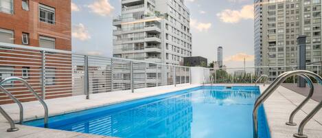 Une piscine sur le toit, entourée de garde-corps en métal, et bordée d’immeubles de grande hauteur.