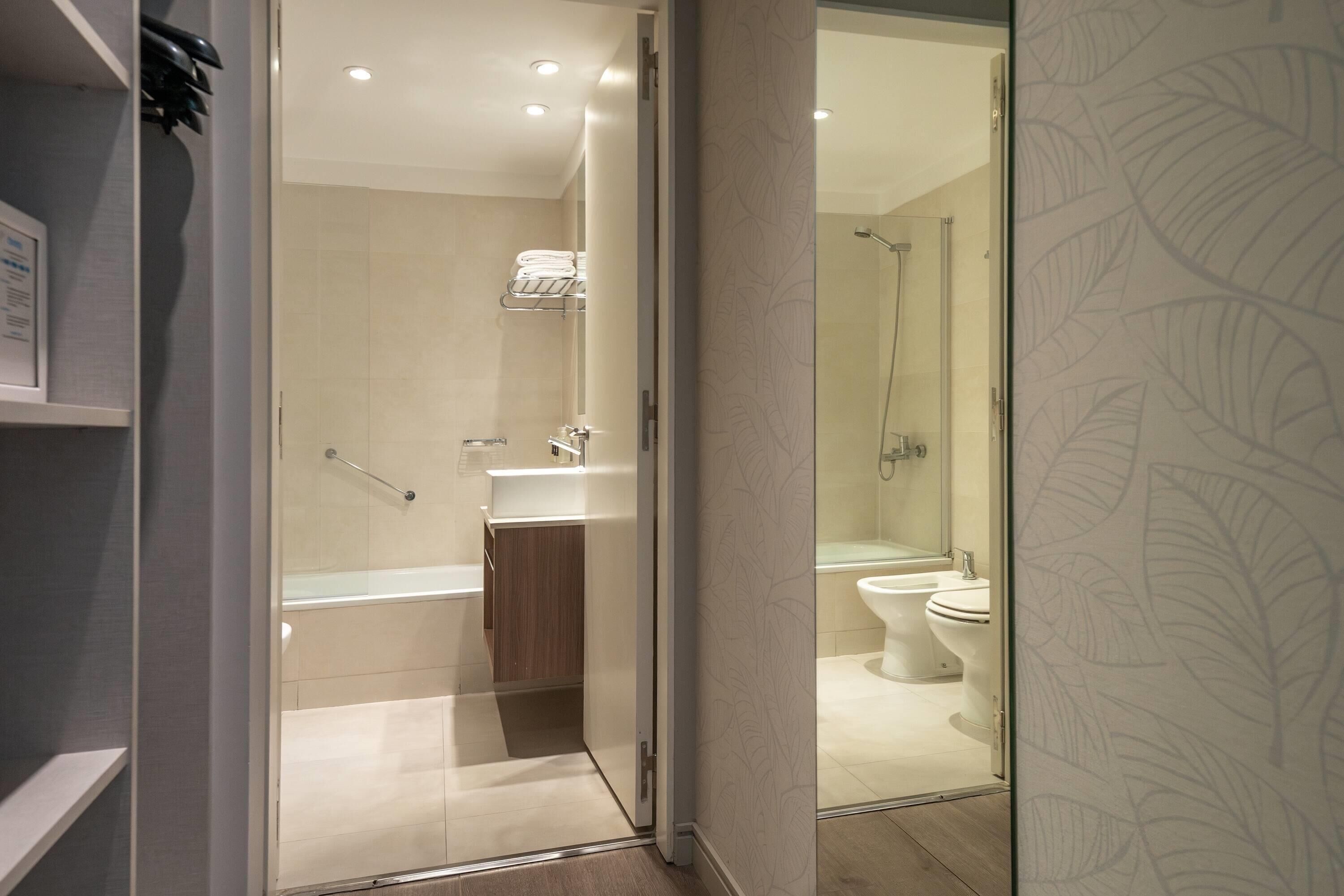 Un baño moderno con cabina de ducha de vidrio, tocador de madera y retrete blanco.