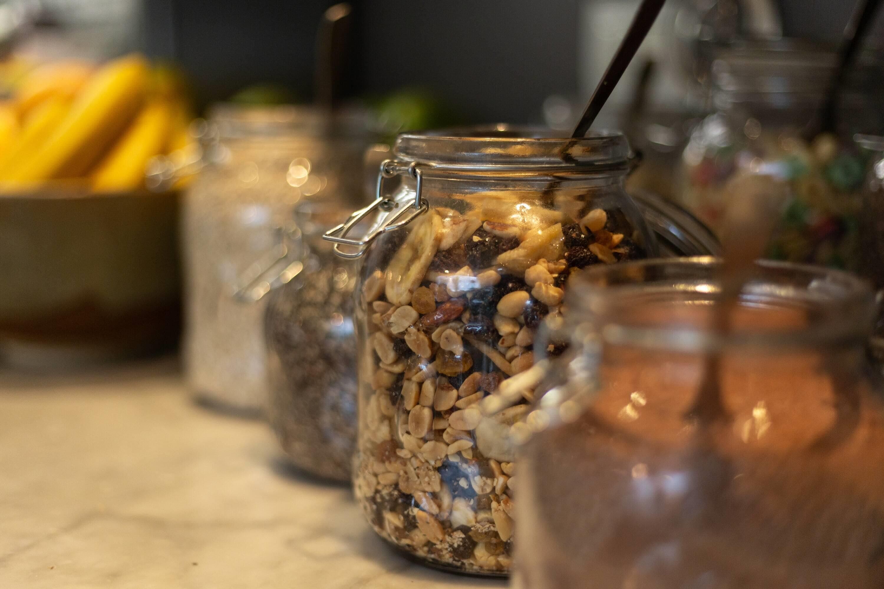Une vue rapprochée de bocaux en verre remplis d’un mélange de noix et de fruits secs, probablement utilisés pour préparer du granola ou des en-cas faits maison.