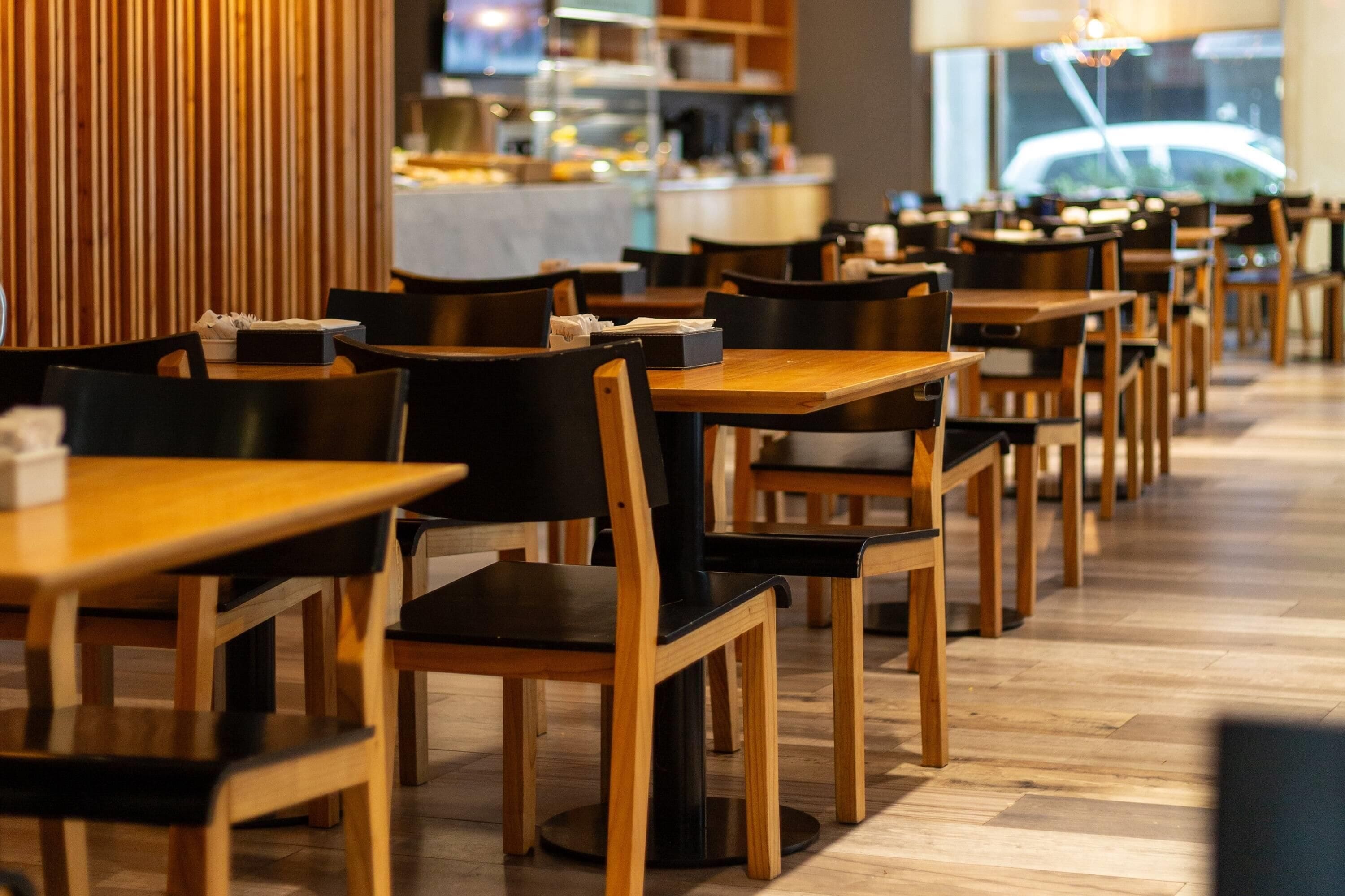 Un restaurante con mesas y sillas de madera, una cocina al fondo y vistas a la calle.