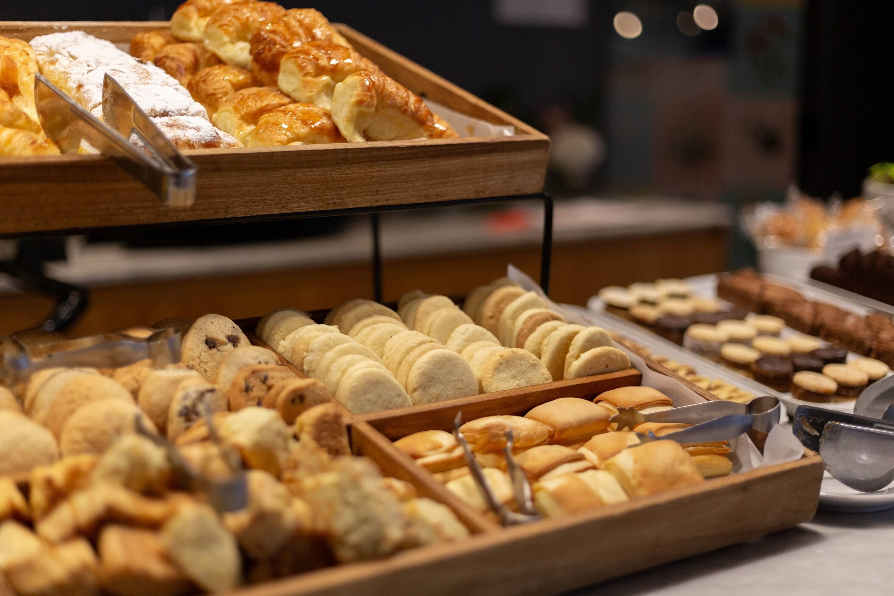 Diversas opciones de productos horneados exhibidos en bandejas de madera, incluyendo pasteles y galletas.