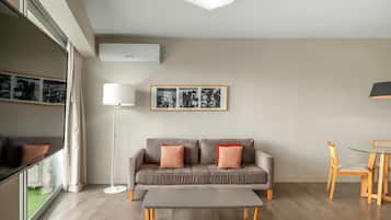 Una sala moderna con un sofá gris, una lámpara de pie, una mesa de centro, una mesa de comedor con sillas y un cuadro enmarcado en la pared.