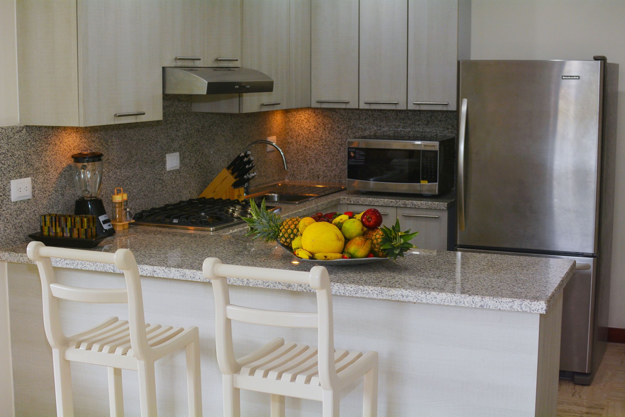 Una cocina con encimeras de granito, electrodomésticos de acero inoxidable y un frutero en la isla.