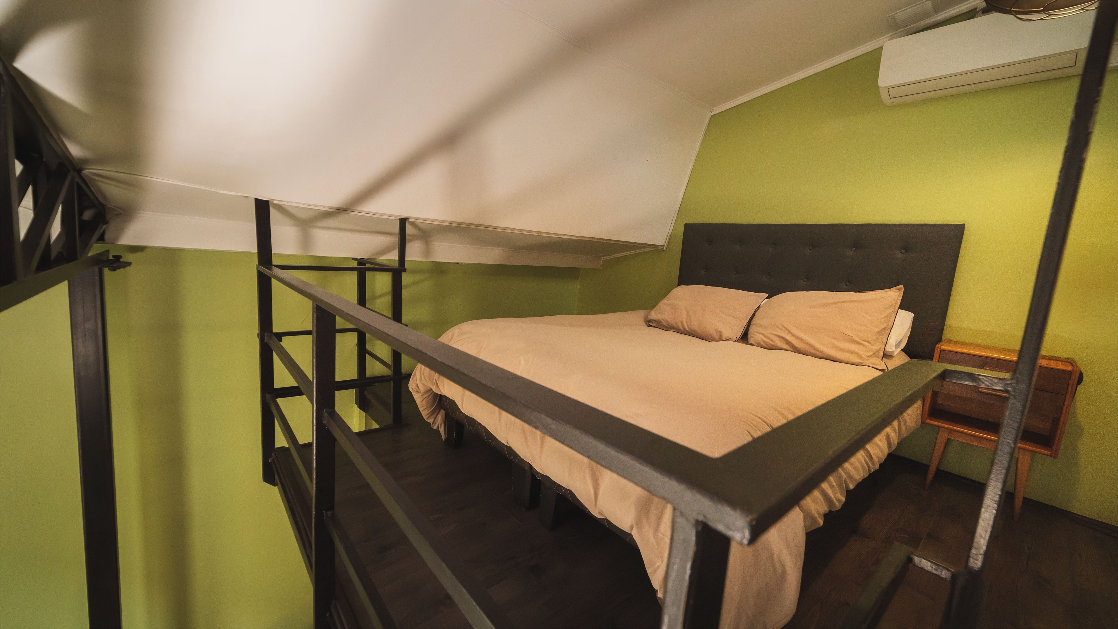 Una cama litera con cabecera, una mesita de noche y una unidad de aire acondicionado encima.