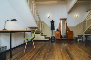 A spacious room with a wooden floor, a green chair, a desk with a lamp, and a staircase with a wooden railing. - La Joya Hostel (Valparaiso)