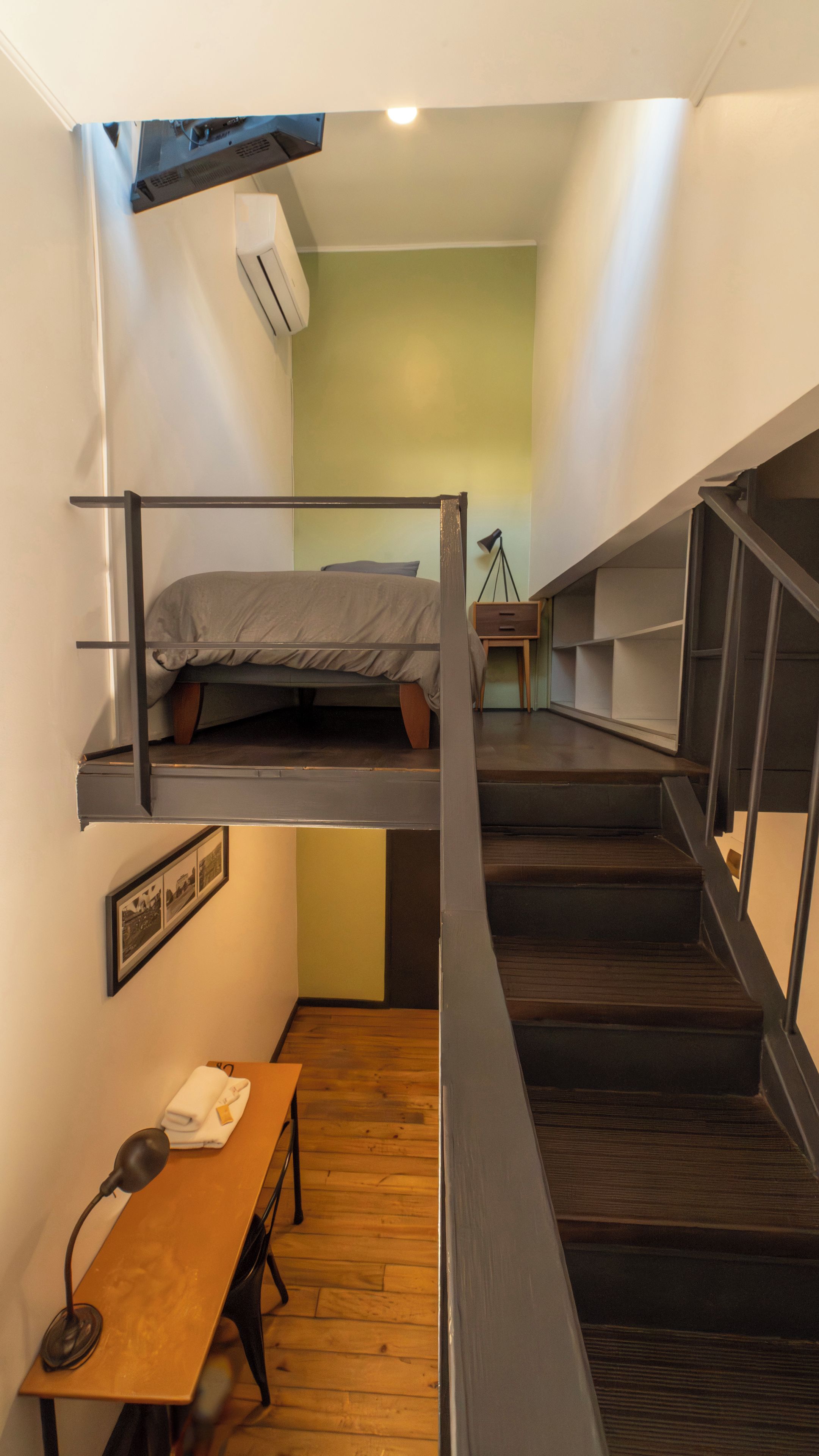 Una habitación compacta con una cama individual superpuesta, un escritorio con silla y una pequeña mesa con lámpara.