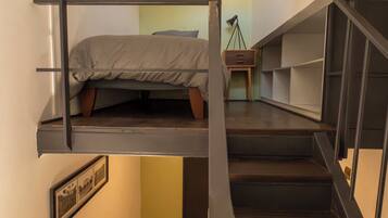 A compact room with a bunk bed, a desk with a chair, and a small table with a lamp.