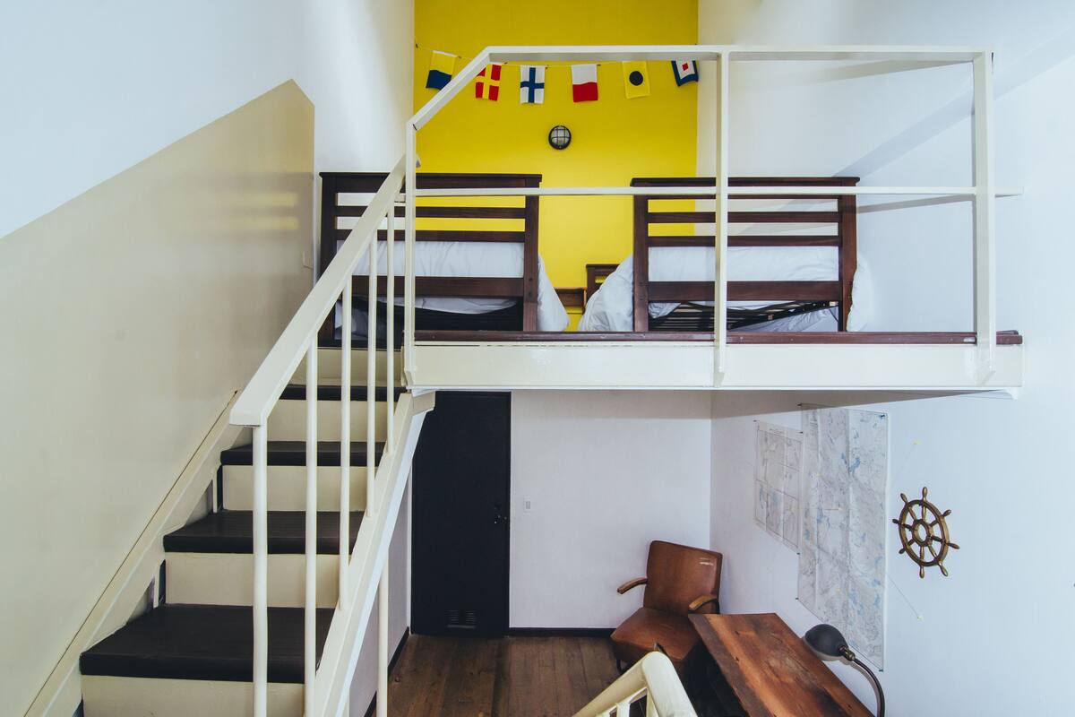 A dormitory-style room with bunk beds, a desk, and a chair.