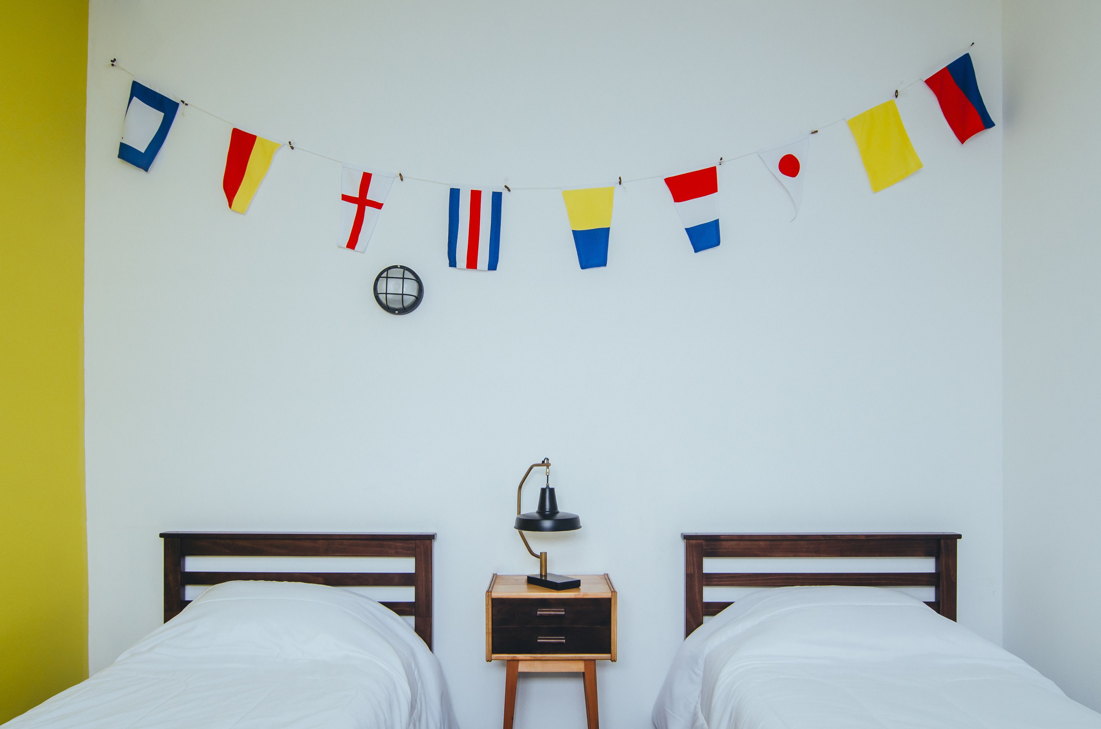 Quarto com duas camas, mesa de cabeceira com abajur e parede decorada com uma guirlanda de bandeiras.