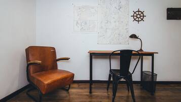 A room with a wooden floor, a brown leather chair, a black chair, a wooden desk, a ship's wheel decoration, and a map on the wall.