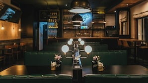 A bar area with a long counter, green seating, and a hanging light fixture. - La Joya Hostel (Valparaiso)