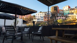 An outdoor seating area with chairs and tables, overlooking a cityscape with buildings of various colors and architectural styles. - La Joya Hostel (Valparaiso)