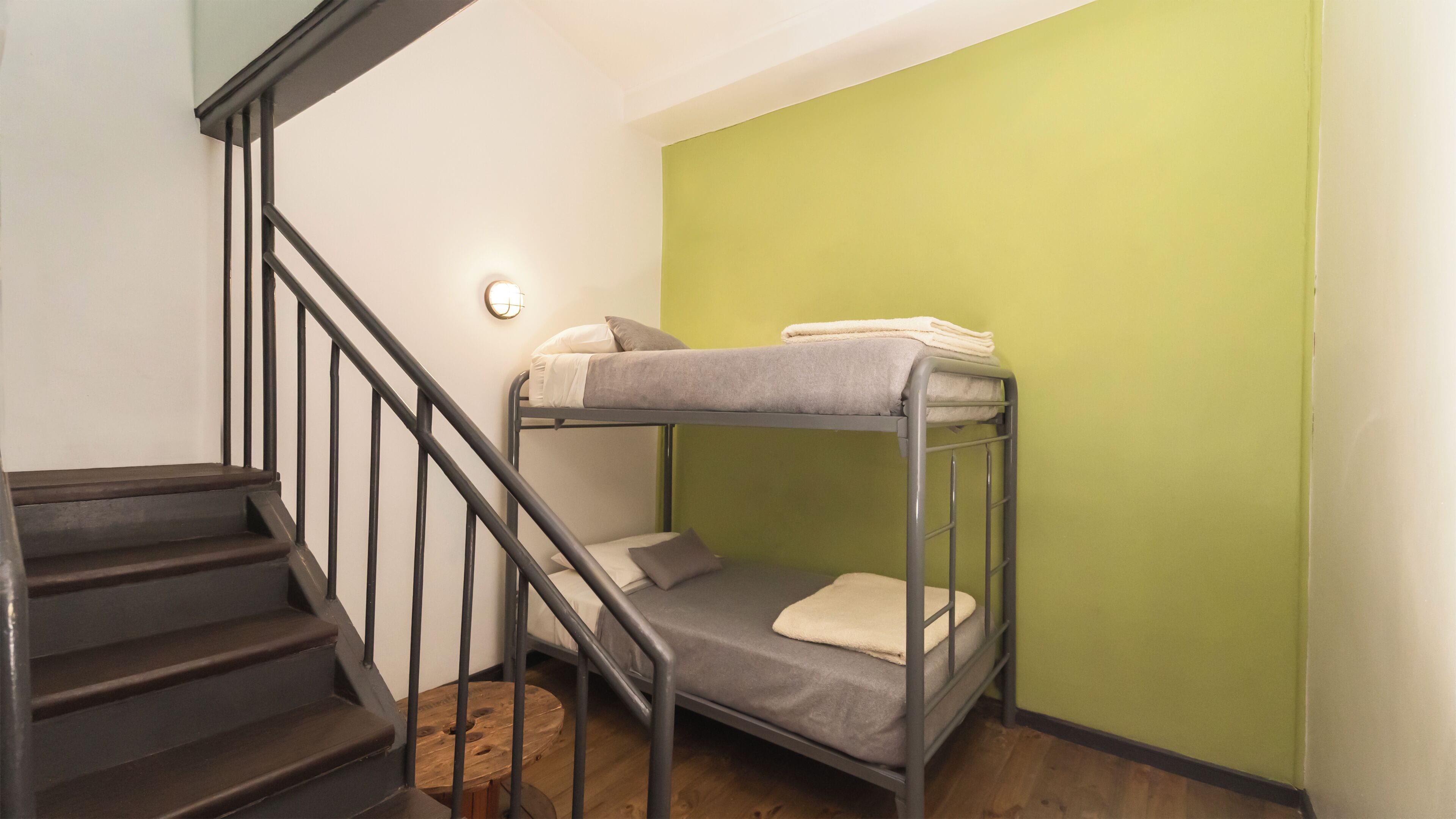 Una cama litera en una habitación con escaleras y pared verde.