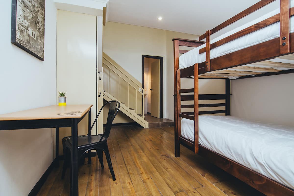 A bunk bed room with a desk and chair, a staircase, and a framed picture on the wall.