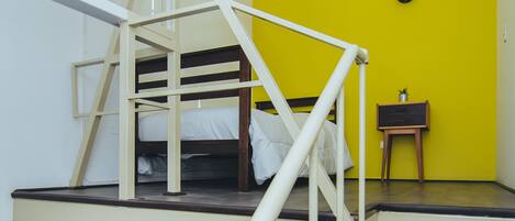 A bunk bed with a white railing, a small table with a plant, and a yellow wall with flags.