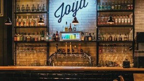 A bar area with a 'Joya' sign, shelves of liquor bottles, a bar counter, and green seating. - La Joya Hostel (Valparaiso)