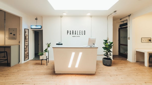 A modern reception desk with a minimalist design, a visible nameplate, and potted plants. - La Joya Hostel (Valparaiso)