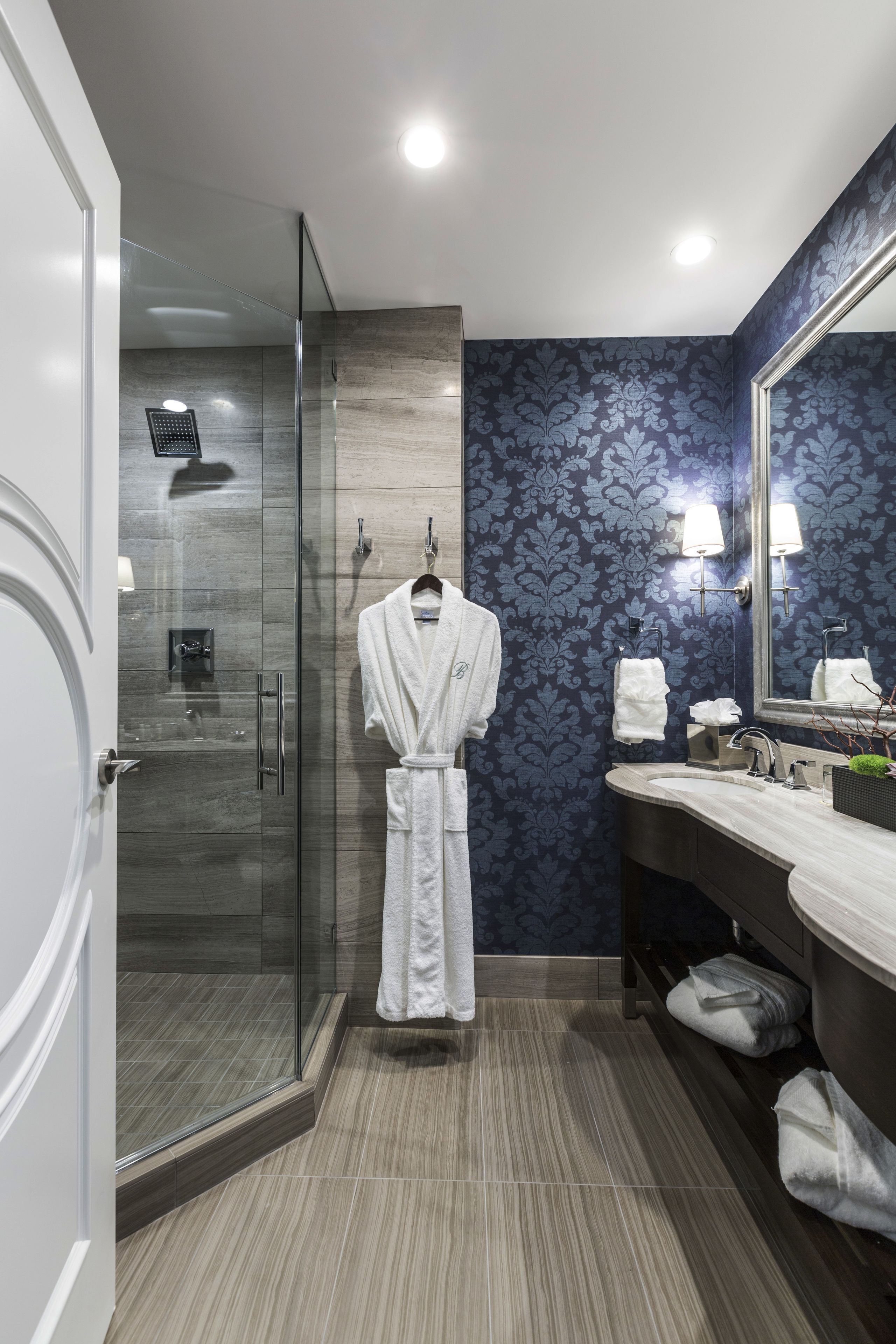 A modern bathroom with a glass-enclosed shower, a large mirror, and a vanity with a sink and towel rack.