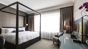 A four-poster bed with a dark frame, a desk with a computer, a television, and a potted plant. - La Banque Hotel (Homewood)