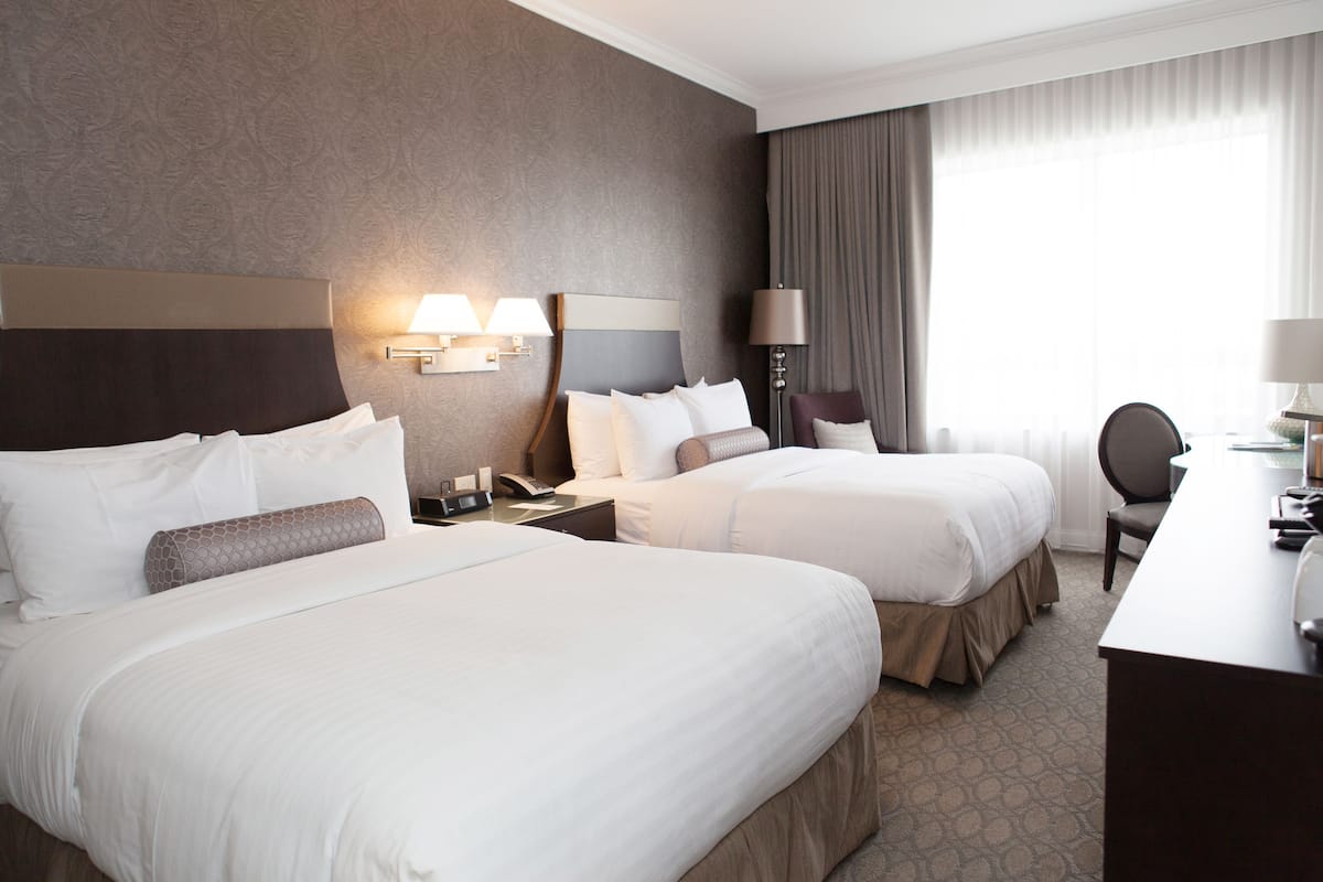 A hotel room with two large beds, a desk, a chair, and a lamp.