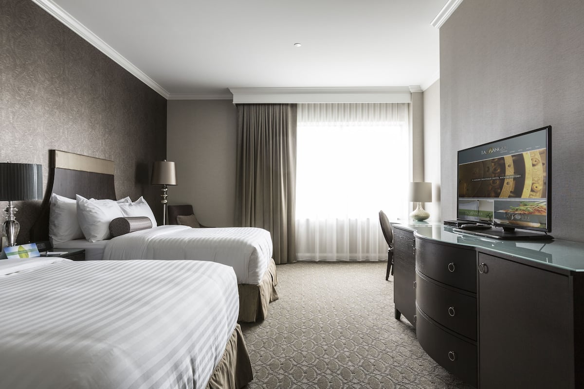A hotel room with two beds, a desk with a television, and a large window with curtains.