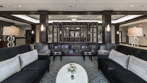 A lobby with two black sofas, a coffee table, and a bookshelf filled with books. - La Banque Hotel (Homewood)