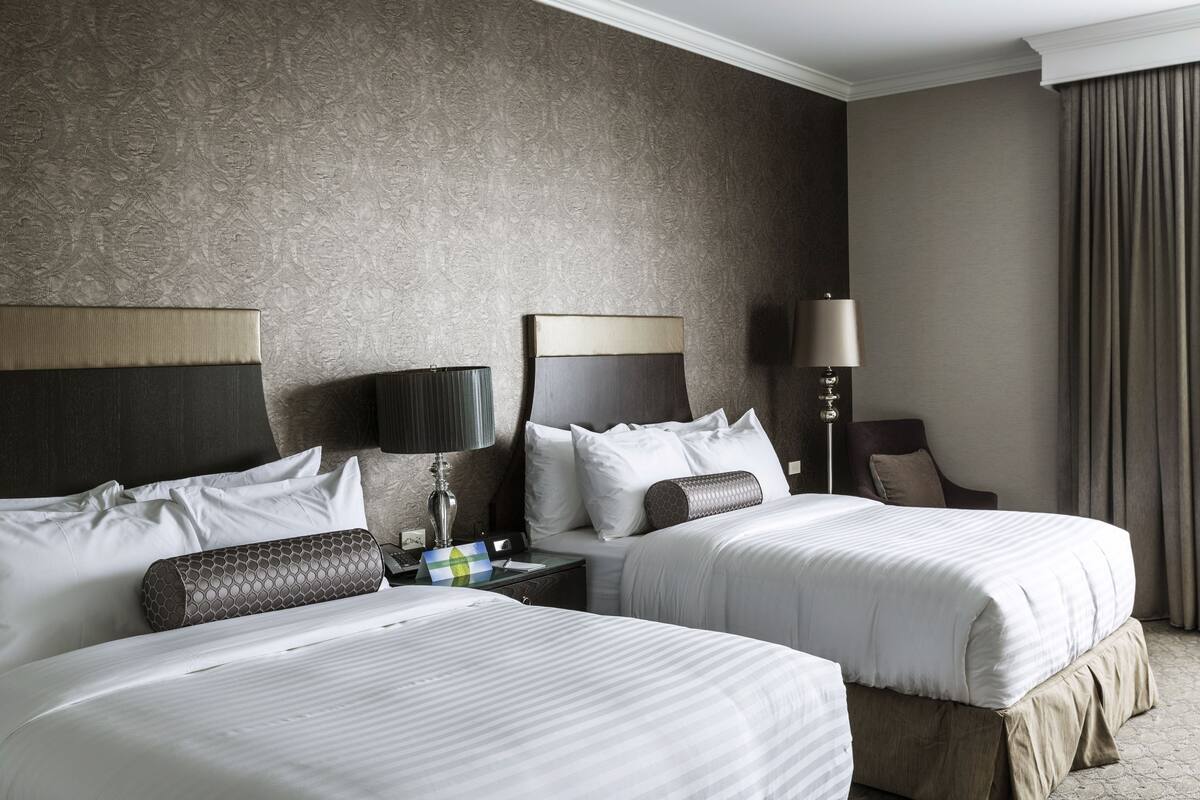 A hotel room with two beds, a nightstand, a lamp, and a chair.
