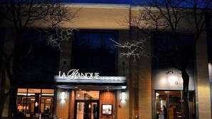 The exterior of La Banque Hotel with a well-lit entrance, a visible signboard, and a potted plant in front. - La Banque Hotel (Homewood)