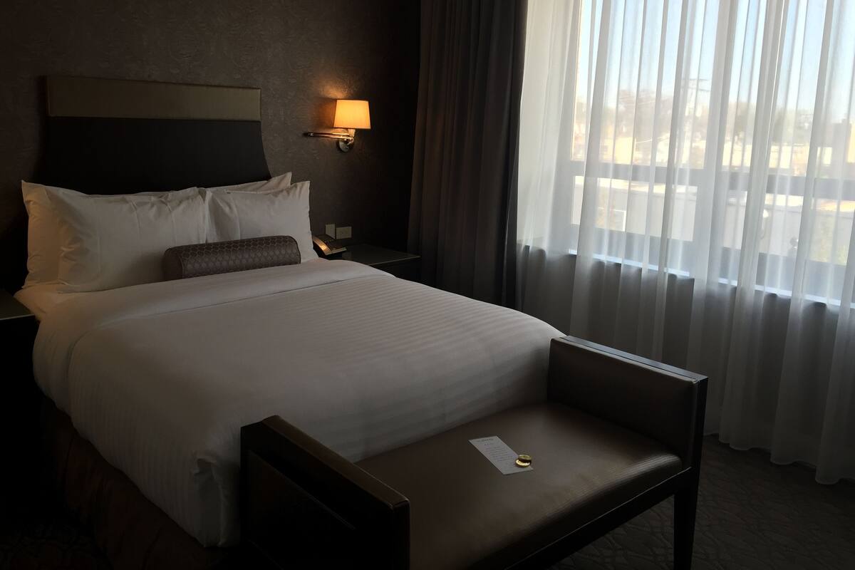 A hotel room with a bed, a nightstand, a lamp, a chair, and a window with curtains.