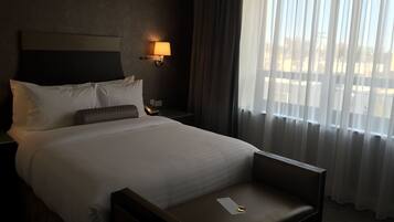 A hotel room with a bed, a nightstand, a lamp, a chair, and a window with curtains.