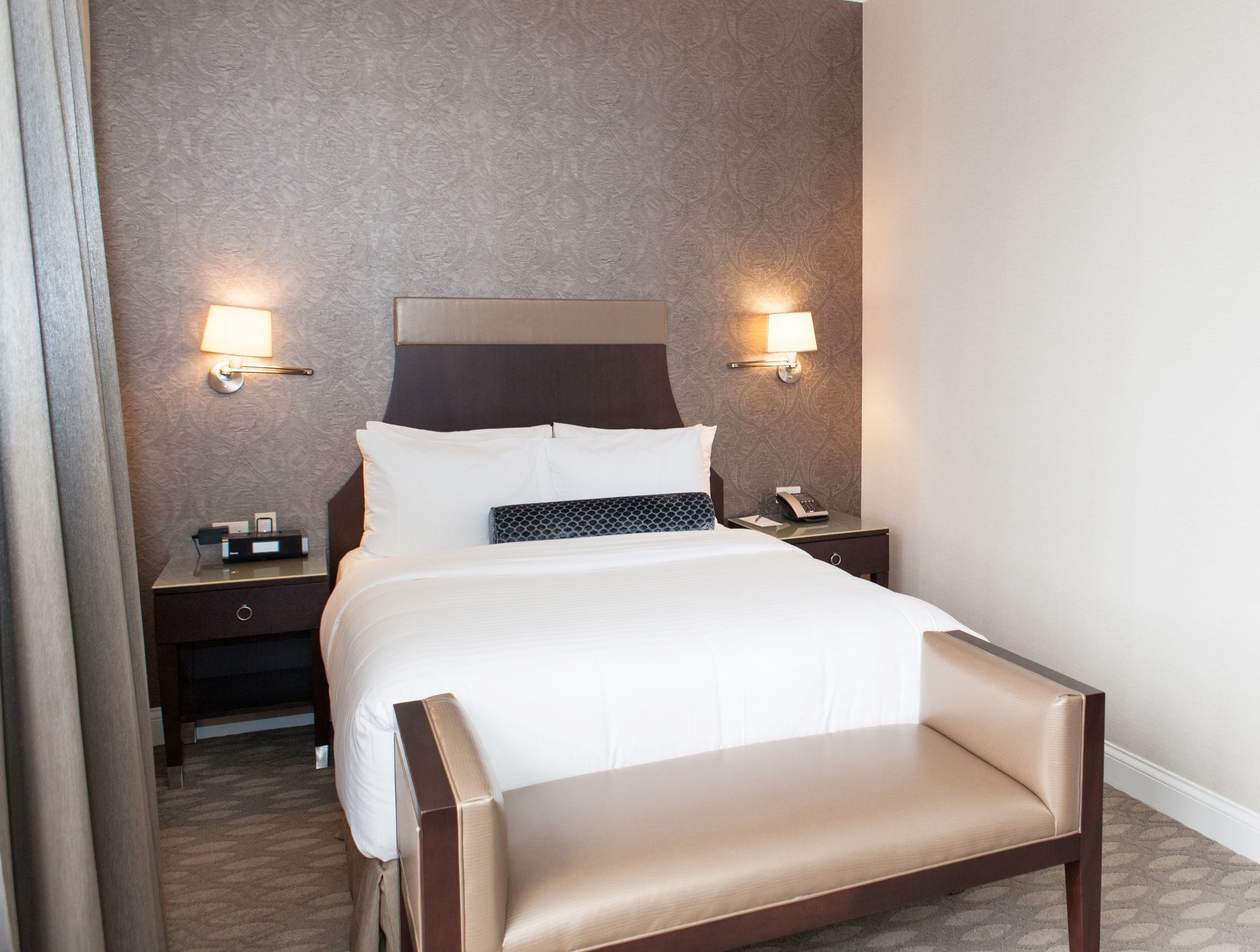 Ein Hotelzimmer mit einem großen Bett, zwei Nachttischen, einer Kopfteil und Wandlampen.