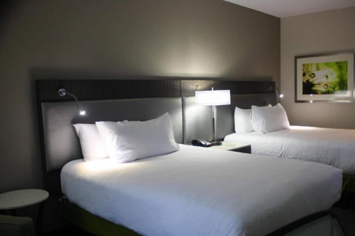 A hotel room with two beds, bedside tables, lamps, and a painting on the wall.