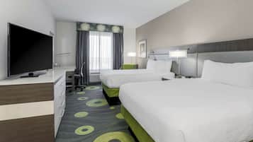 A hotel room with two beds, a desk with a flat-screen TV, a chair, a lamp, and a window with curtains.