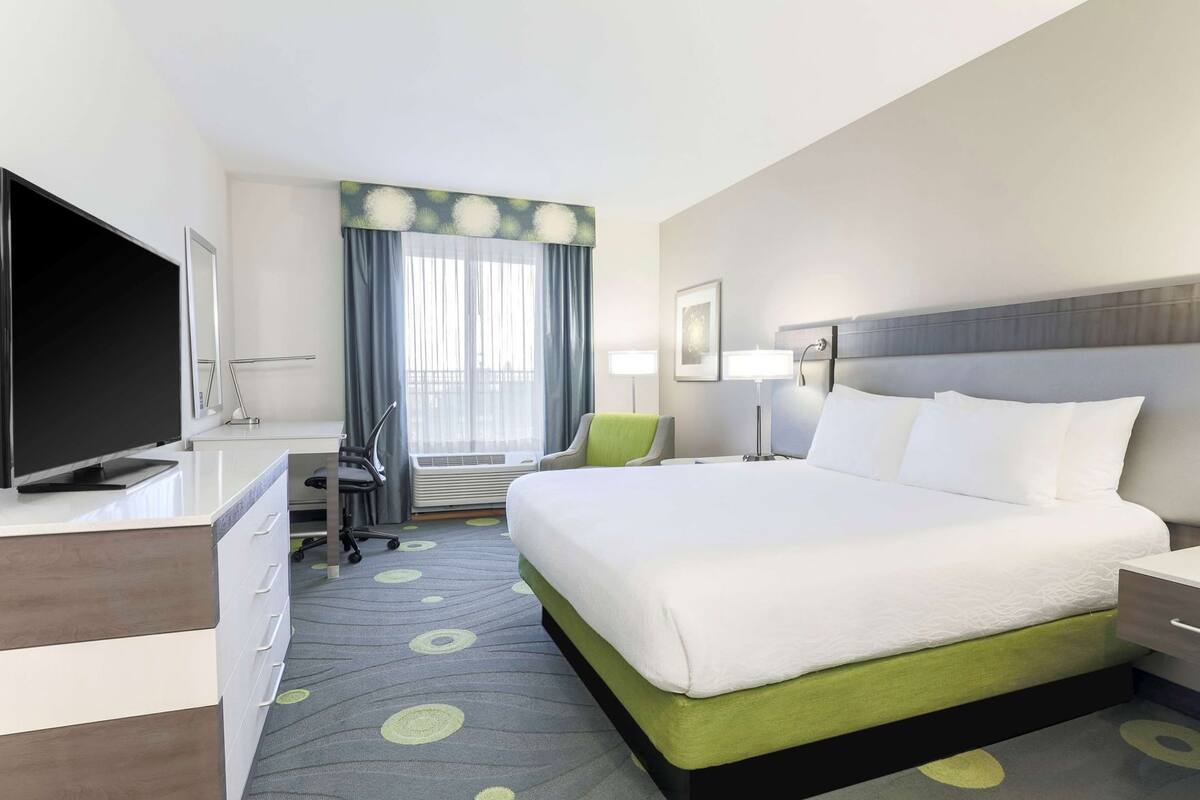 A hotel room with a bed, desk, chair, TV, and a window with curtains.