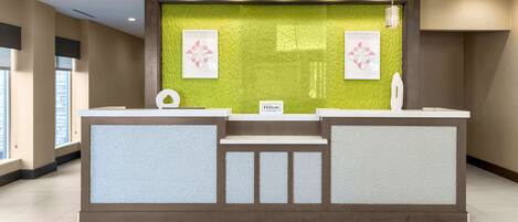 A reception desk with a green textured wall, two framed floral artworks, and a sign reading "Hilton."