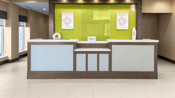 Un mostrador de recepción con una pared texturizada verde, dos cuadros con motivos florales y un cartel que dice "Hilton".