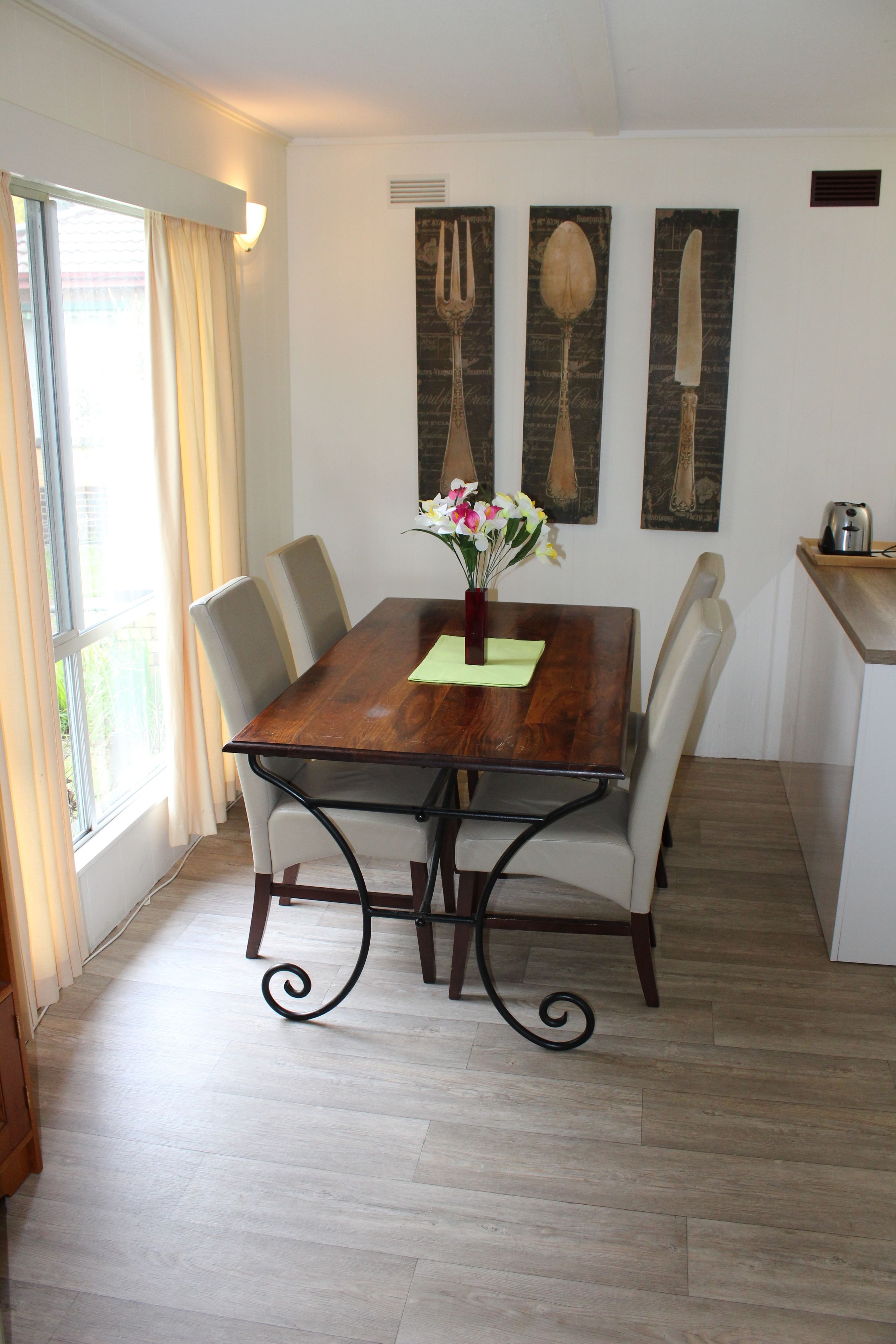 A dining area with a wooden table, white chairs, a vase with flowers, and artwork on the wall.