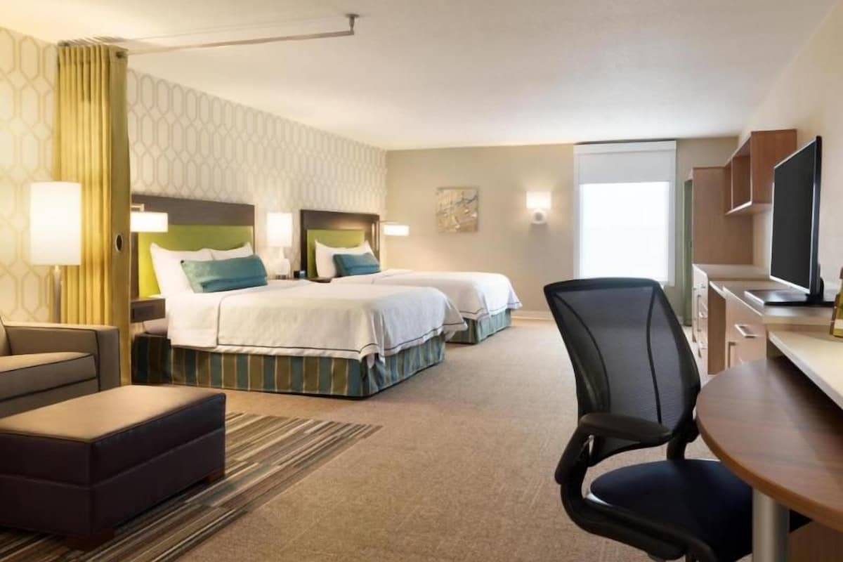 Une chambre d’hôtel avec deux lits, un bureau, une chaise, une télévision et une fenêtre.