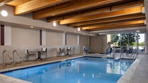 Une piscine intérieure avec des poutres en bois, des murs carrelés et des espaces aménagés pour s’asseoir.