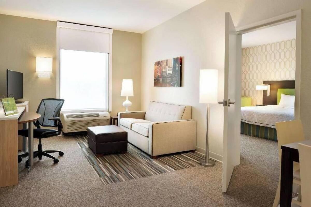 A hotel room with a sofa, a desk with a chair, a lamp, a bed, and a television.