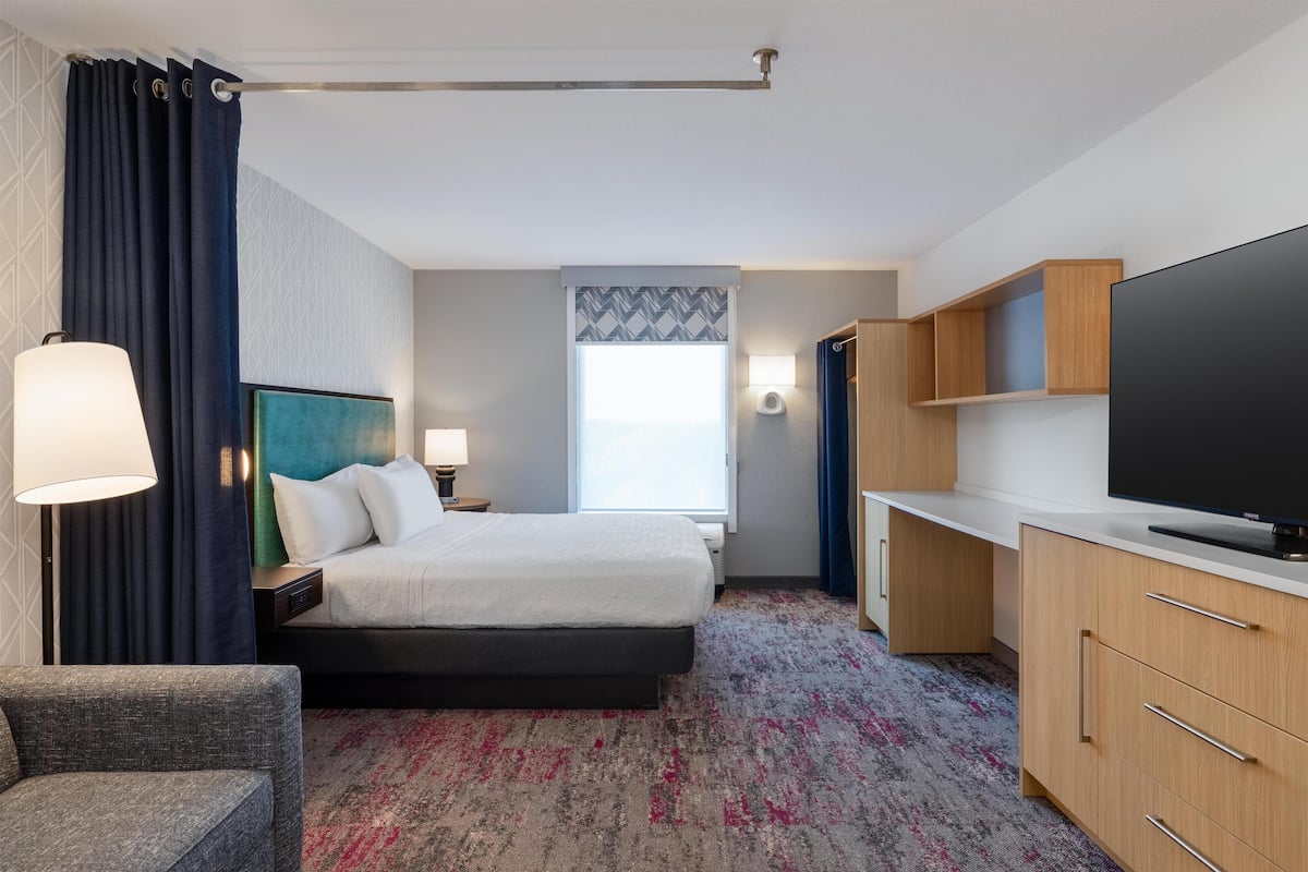 A hotel room with a bed, a desk, a TV, and a chair.