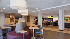 Un hall d’hôtel moderne doté d’espaces aménagés avec des sièges, d’un bar et d’un téléviseur.