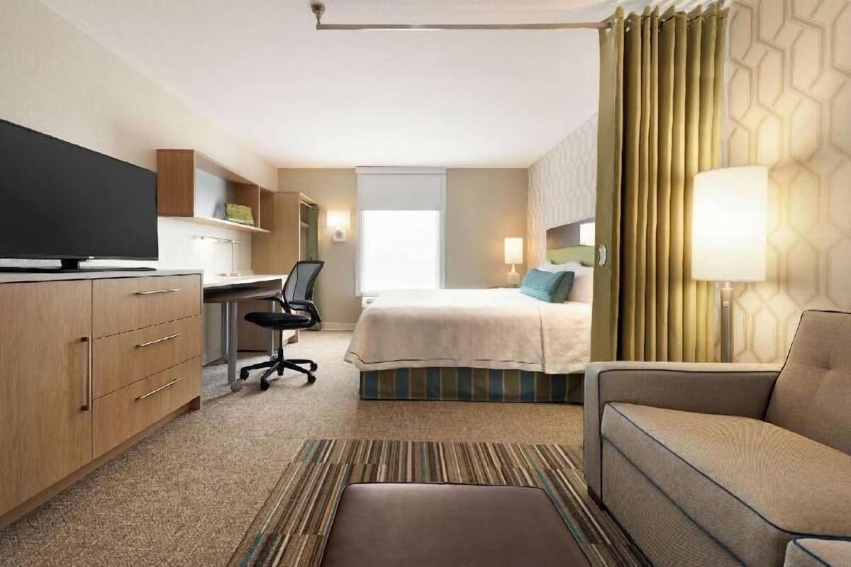 A hotel room with a bed, a desk, a chair, a TV, and a sofa.